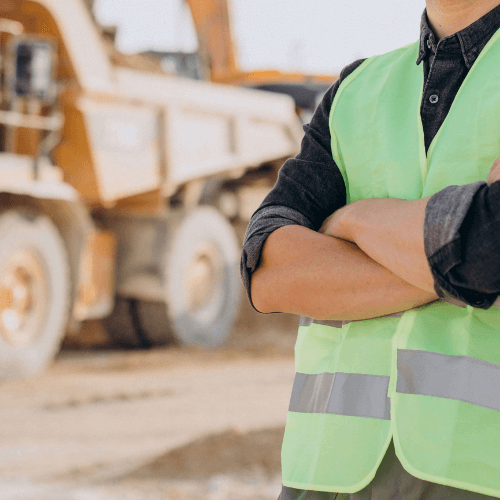 Homem branco de roupa de sinalização de construção em uma obra com um caminhão de obras ao fundo